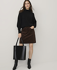 A woman wearing a black sweater, leopard-print skirt, and black boots stands holding a black tote bag against a plain white background. carousel Product Image 1