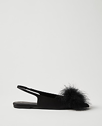 A black flat shoe with a fluffy pom-pom sits in the foreground against a plain, light gray background. carousel Product Image 1