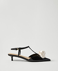 A black patent leather kitten heel with a cream-colored fabric flower on the toe sits against a plain, light gray background. carousel Product Image 1