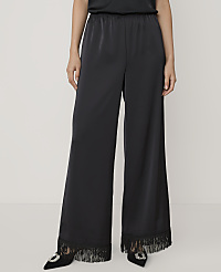 A person wears wide-leg black satin trousers with fringed hems and black pointed heels against a plain light grey background. carousel Product Image 2
