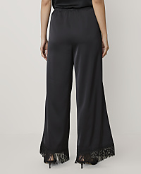 A person stands facing away from the camera wearing wide-leg black satin trousers with fringe hems against a plain light grey background. carousel Product Image 3