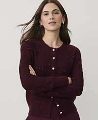 A woman with long brown hair wearing a sparkling burgundy cardigan stands with her arms crossed against a plain light gray background. carousel Product Image 1
