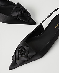 Two black satin pointed-toe heels with rose accents are positioned diagonally against a plain white background. carousel Product Image 2