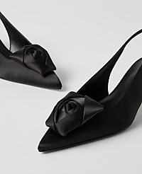 A pair of black satin slingback heels with rose-shaped ornaments on the toes are set against a plain light gray background. carousel Product Image 2