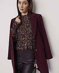 A woman wearing a patterned blouse, dark leather trousers, and a burgundy coat stands against a plain white background. carousel Product Image 4