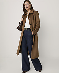 A woman wearing a long brown coat, white shirt, and wide-leg dark blue jeans stands against a plain, light-colored background. carousel Product Image 1