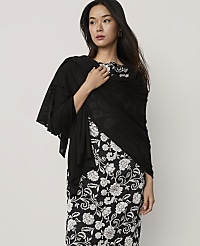 A woman wearing a black shawl over a black and white floral dress stands against a plain light gray background. carousel Product Image 1
