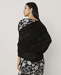 A woman wearing a black and white floral dress and a black shawl stands against a plain light gray background. carousel Product Image 2