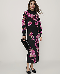 A woman wearing a black floral knit set and black heels stands against a plain, light-colored background. carousel Product Image 1