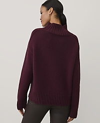 A woman wearing a burgundy ribbed turtleneck sweater and dark brown pants stands against a plain light gray background. carousel Product Image 2