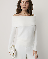 A woman wearing an off-the-shoulder white sweater and white trousers stands against a plain, light-colored background. carousel Product Image 1
