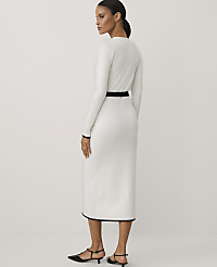 A woman wearing a long-sleeved white dress with black trim and black heels stands against a plain white background. carousel Product Image 2