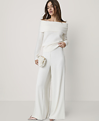 A woman wearing an off-the-shoulder white sweater and wide-leg white trousers stands against a plain, light-colored background. carousel Product Image 1