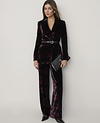 A woman wearing a dark purple velvet floral suit and holding a black clutch stands against a plain white background. carousel Product Image 1