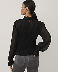 A woman wearing a black smocked blouse and grey jeans stands against a plain light grey background. carousel Product Image 2