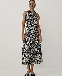 A woman wearing a black and white floral print dress and black heels stands against a plain white background. carousel Product Image 1