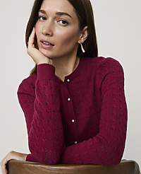 A woman in a textured magenta cardigan rests her chin on her hand against a plain, light-colored background. carousel Product Image 3