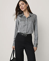 A woman wearing a grey plaid shirt and black trousers stands against a plain, light-colored background. carousel Product Image 1