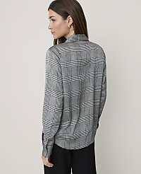 A woman wearing a grey plaid shirt and black trousers stands against a plain, light-colored background. carousel Product Image 2