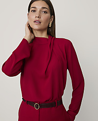 A woman wearing a red long-sleeved top and matching trousers with a dark brown belt stands against a plain, light-colored background. carousel Product Image 1