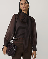 A woman wearing a sheer brown pussy-bow blouse and checkered trousers stands against a plain light grey background. carousel Product Image 1
