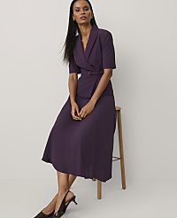 A woman wearing a purple short-sleeved blazer and matching skirt leans against a wooden stool against a plain white background. carousel Product Image 3