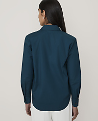 A woman wearing a teal long-sleeved shirt and white trousers stands with her back to the camera against a plain, light-colored background. carousel Product Image 2