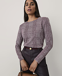 A woman wearing a maroon and white houndstooth top and dark leather trousers stands against a plain, light-colored background. carousel Product Image 1