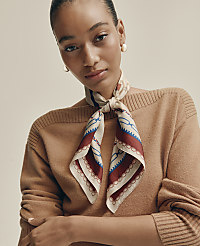 A woman wearing a brown sweater and a patterned silk scarf poses against a plain, neutral-toned background. carousel Product Image 4