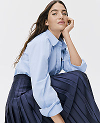 A woman wearing a light blue button-down shirt and a dark navy pleated skirt poses against a plain white background. carousel Product Image 3
