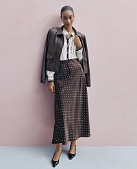 A woman wearing a brown leather jacket, a patterned white shirt, and a polka-dot brown skirt stands against a plain pink wall. carousel Product Image 4