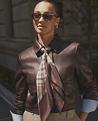 A woman wearing sunglasses, a brown leather jacket, and a patterned scarf stands before a blurred urban building background. carousel Product Image 3