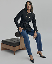 A woman wearing a black double-breasted blazer and blue jeans sits on a modern black leather and wood bench against a plain grey background. carousel Product Image 4