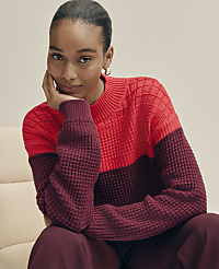 A woman wearing a red and burgundy textured sweater sits against a plain, light-colored background. carousel Product Image 3