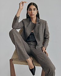 A woman wearing a brown plaid suit and black heels sits in a woven chair against a plain light gray background. carousel Product Image 8