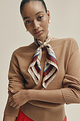 A woman wearing a tan sweater and a patterned silk scarf poses against a plain, light-colored background. carousel Product Image 3