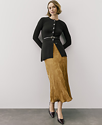A woman wearing a black button-down cardigan and a gold patterned skirt stands against a plain light gray wall. carousel Product Image 1