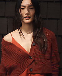 A woman wearing a red cardigan and dress stands against a dark, textured shingle wall. carousel Product Image 5