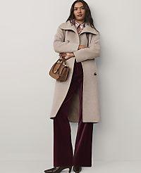 A woman wearing a long beige coat and burgundy velvet trousers stands against a plain white background. carousel Product Image 4