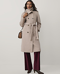 A woman wearing a beige belted coat and burgundy velvet trousers stands against a plain white background. carousel Product Image 1