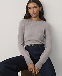 A woman wearing a grey sweater and dark blue jeans sits against a plain white background. carousel Product Image 1