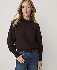A blonde woman wearing a dark brown sweater and blue jeans stands against a plain white background. carousel Product Image 1