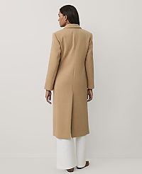 A woman stands with her back to the camera wearing a long camel-colored coat and white wide-leg trousers against a plain light gray background. carousel Product Image 2