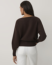 A woman wearing a brown sweater and white pants stands with her back to the camera against a plain light gray background. carousel Product Image 2