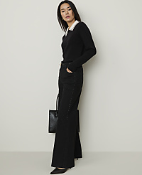 A woman wearing a black sweater with a white collar and wide-leg black trousers stands against a plain, light-colored wall. carousel Product Image 1