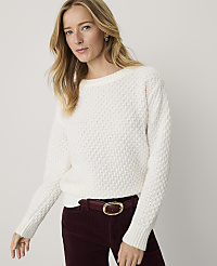 A blonde woman wearing a white textured sweater and maroon corduroy pants stands against a plain light gray background. carousel Product Image 1