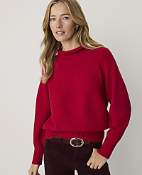 A woman wearing a bright red sweater and dark corduroy pants stands against a plain, light-colored background. carousel Product Image 1