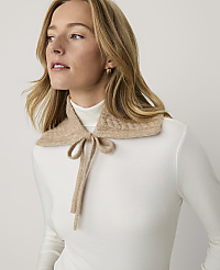A blonde woman wearing a white turtleneck and a beige knit collar stands against a plain white background. carousel Product Image 1