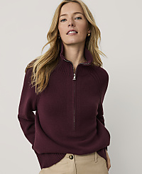 A blonde woman wearing a maroon quarter-zip sweater and khaki pants stands against a plain, light-colored background. carousel Product Image 1