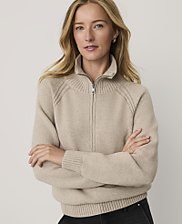 A woman with blonde hair wearing a beige zip-up sweater stands with her arms crossed against a plain, light-colored background. carousel Product Image 1